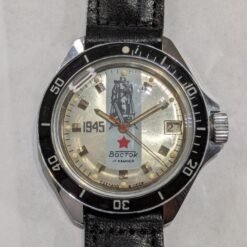 Orologio Vostok Komandirskie commemorativo 1945, quadrante argentato con statua della Vittoria, ghiera in bachelite nera, movimento meccanico manuale Vostok 2414, cassa in ottone cromato, cinturino sovietico originale.