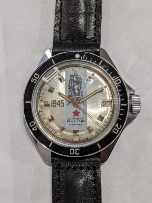 Orologio Vostok Komandirskie commemorativo 1945, quadrante argentato con statua della Vittoria, ghiera in bachelite nera, movimento meccanico manuale Vostok 2414, cassa in ottone cromato, cinturino sovietico originale.