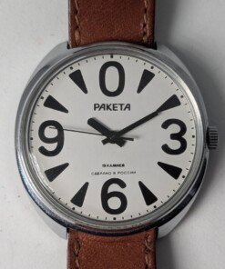 Raketa Big Zero Russo – Scatola e Cinturino Originali Importatore – Grade B 16 Orologio da polso Raketa Big Zero russo con quadrante bianco, numeri arabi neri (0, 3, 6, 9), lancette nere e cinturino in pelle marrone originale, presentato con la sua scatola originale.