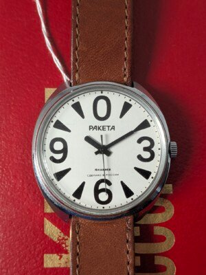 Orologio da polso Raketa Big Zero russo con quadrante bianco, numeri arabi neri (0, 3, 6, 9), lancette nere e cinturino in pelle marrone originale, presentato con la sua scatola originale.