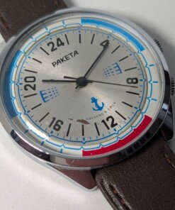 Raketa Marine 24 Ore Sovietico Vintage (Anni '80) Grade C 17 Orologio da polso sovietico Raketa Marine 24 ore vintage degli anni '80 con quadrante argentato, indicazione delle 24 ore, lunetta blu e rossa con simboli marittimi e cinturino in pelle marrone.