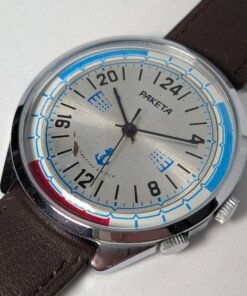 Raketa Marine 24 Ore Sovietico Vintage (Anni '80) Grade C 16 Orologio da polso sovietico Raketa Marine 24 ore vintage degli anni '80 con quadrante argentato, indicazione delle 24 ore, lunetta blu e rossa con simboli marittimi e cinturino in pelle marrone.