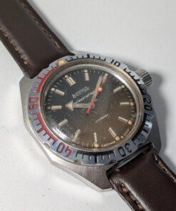 Vostok Amphibia 470 Sovietico Vintage (Anni '80) - Leggenda Subacquea Grade B 13 Orologio subacqueo sovietico vintage Vostok Amphibia 470 degli anni '80 con quadrante scuro, indici luminosi, ghiera girevole numerata e cinturino in pelle marrone.