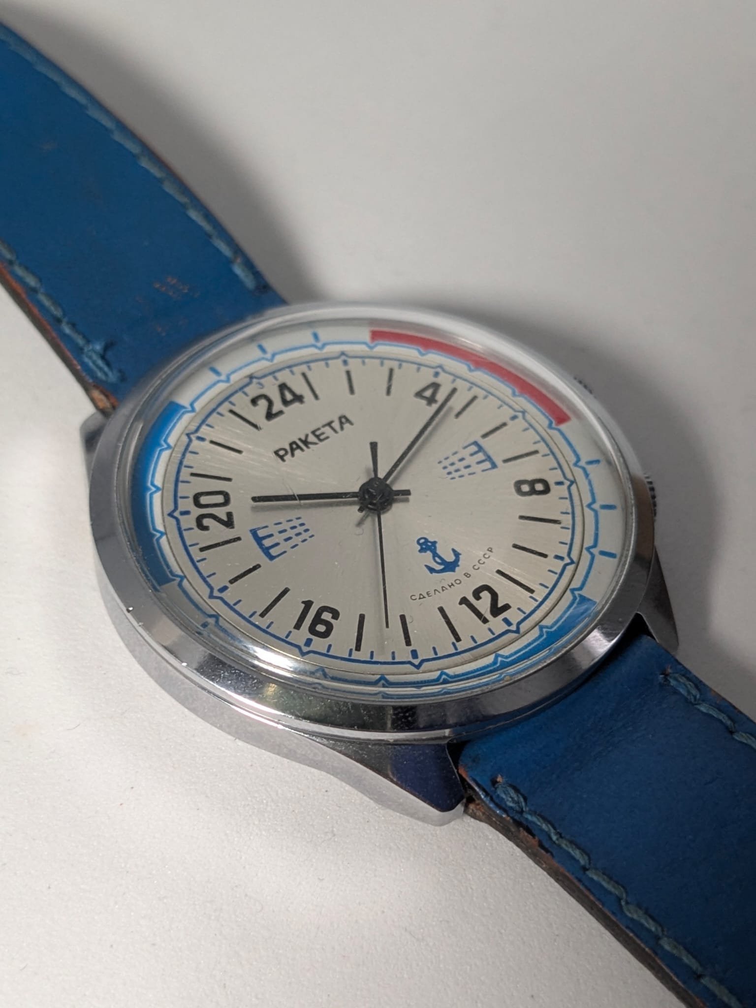Orologio Sovietico Raketa Marine 24h con Cinturino Originale Blu - Grade B 5 Orologio sovietico Raketa Marine 24 ore anni '80 con quadrante argentato, linee blu tratteggiate per silenzio radio e cinturino blu