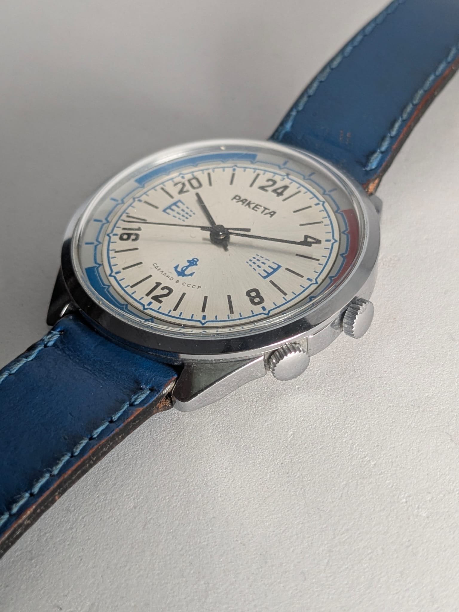 Orologio Sovietico Raketa Marine 24h con Cinturino Originale Blu - Grade B 2 Orologio sovietico Raketa Marine 24 ore anni '80 con quadrante argentato, linee blu tratteggiate per silenzio radio e cinturino blu