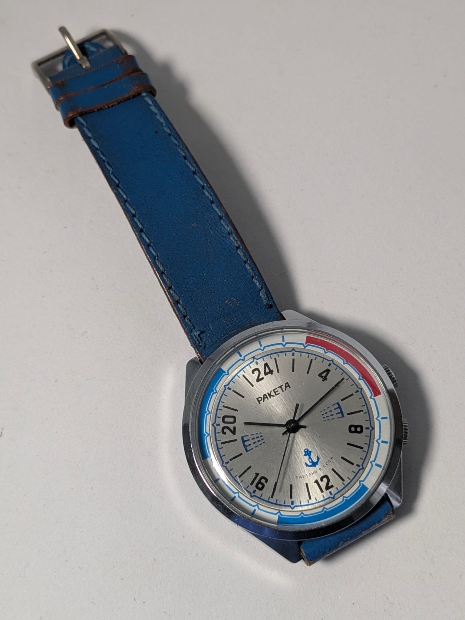 Orologio Sovietico Raketa Marine 24h con Cinturino Originale Blu - Grade B 9 Orologio sovietico Raketa Marine 24 ore anni '80 con quadrante argentato, linee blu tratteggiate per silenzio radio e cinturino blu