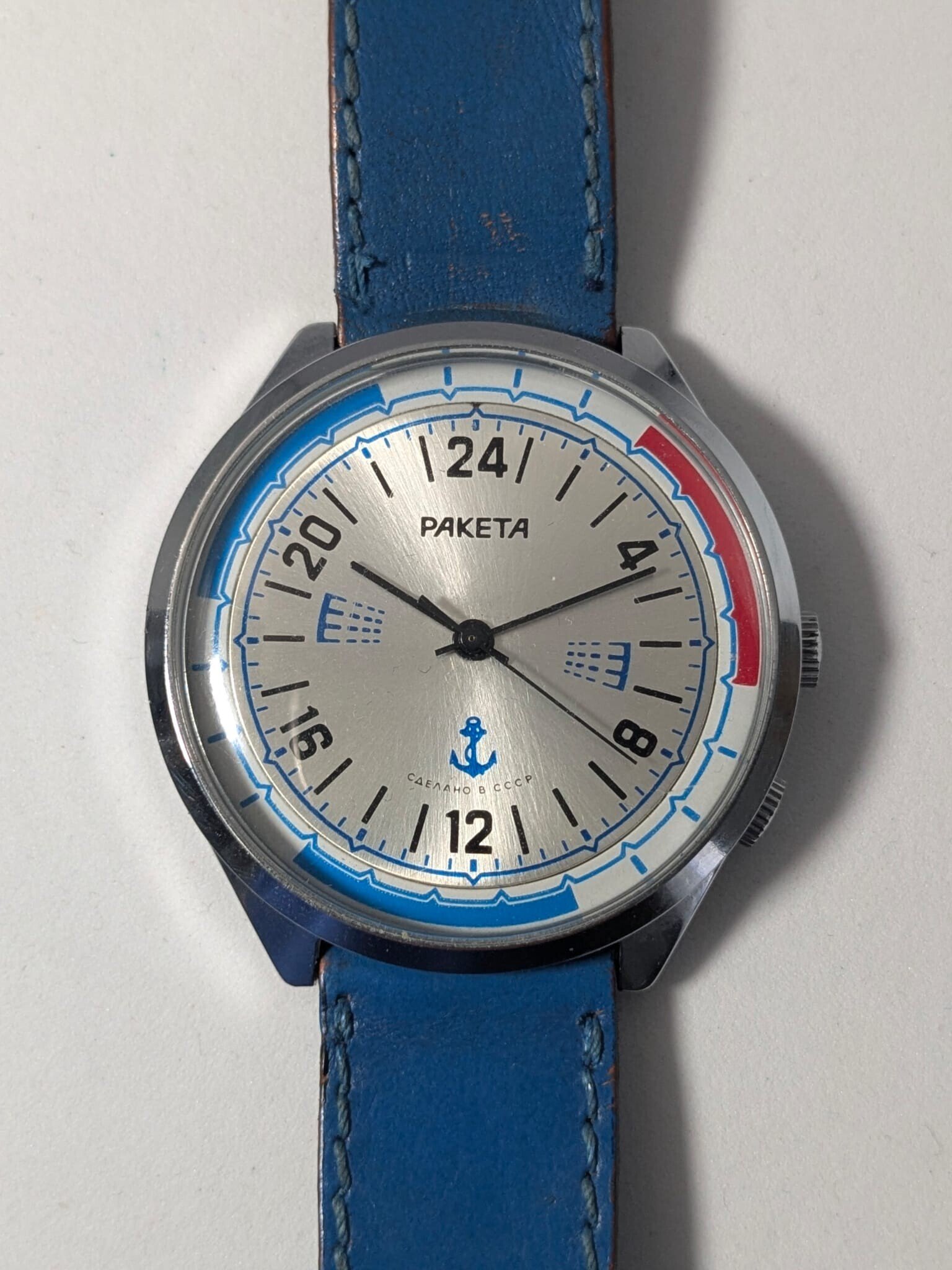 Orologio Sovietico Raketa Marine 24h con Cinturino Originale Blu - Grade B 1 Orologio sovietico Raketa Marine 24 ore anni '80 con quadrante argentato, linee blu tratteggiate per silenzio radio e cinturino blu