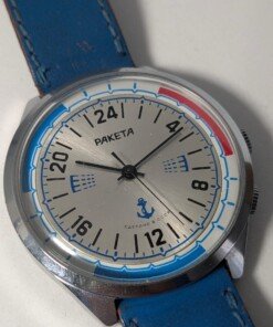 Orologio Sovietico Raketa Marine 24h con Cinturino Originale Blu - Grade B 19 Orologio sovietico Raketa Marine 24 ore anni '80 con quadrante argentato, linee blu tratteggiate per silenzio radio e cinturino blu