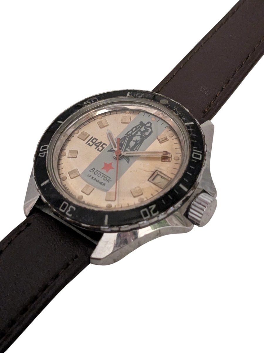 Orologio Vostok Komandirskie Della Vittoria – Meccanico Manuale 2414 - Grade B 5 Orologio russo Vostok Komandirskie vintage da collezione, quadrante crema 1945 con soldato, lunetta nera girevole e cinturino marrone, vista frontale destra.