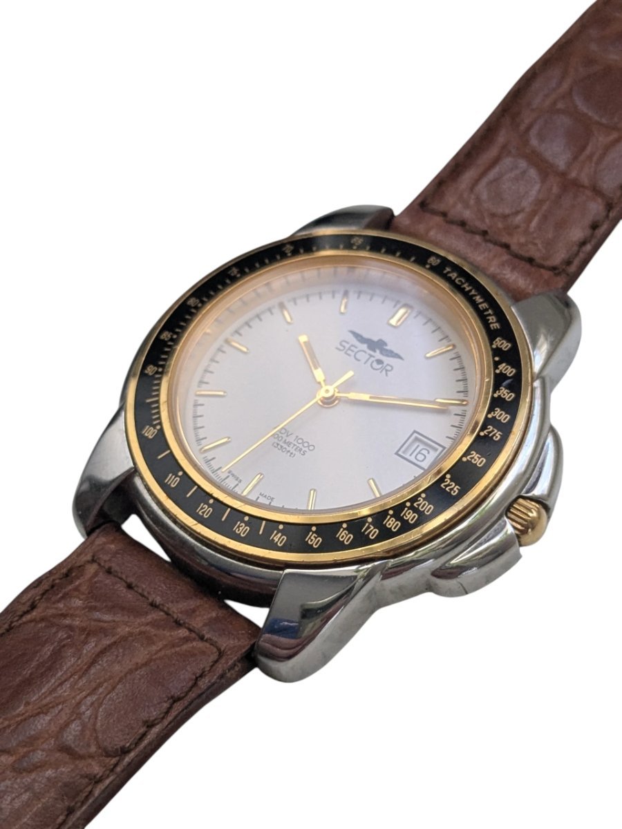 Orologio Sector ADV 1000 Quartz Anni ’90 Tachimetro Swiss Made - Grade B 8 Orologio Sector DV 1000 vintage Swiss Made con quadrante argento, dettagli dorati, lunetta tachimetrica e datario. Cinturino in pelle marrone.