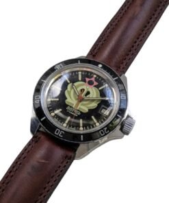 Orologio Vostok Amphibia vintage russo, ref. 250, con quadrante nero a motivo vegetale verde, stella rosa e datario. Lunetta girevole e cinturino in pelle marrone.