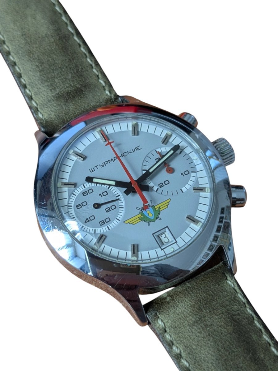 Orologio Sturmanskie Cronografo Calibro 3133 Anni 90 Russia 6 Orologio cronografo vintage russo Poljot Sturmanskie 3133 con quadrante argento, emblematico logo aeronautico e cinturino in pelle verde.